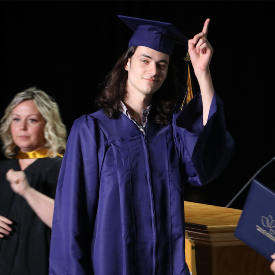 A graduate walking across the stage holding up the number 1 gesture